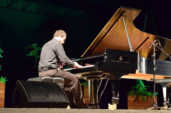 Homem de roupa cinza tocando piano no palco