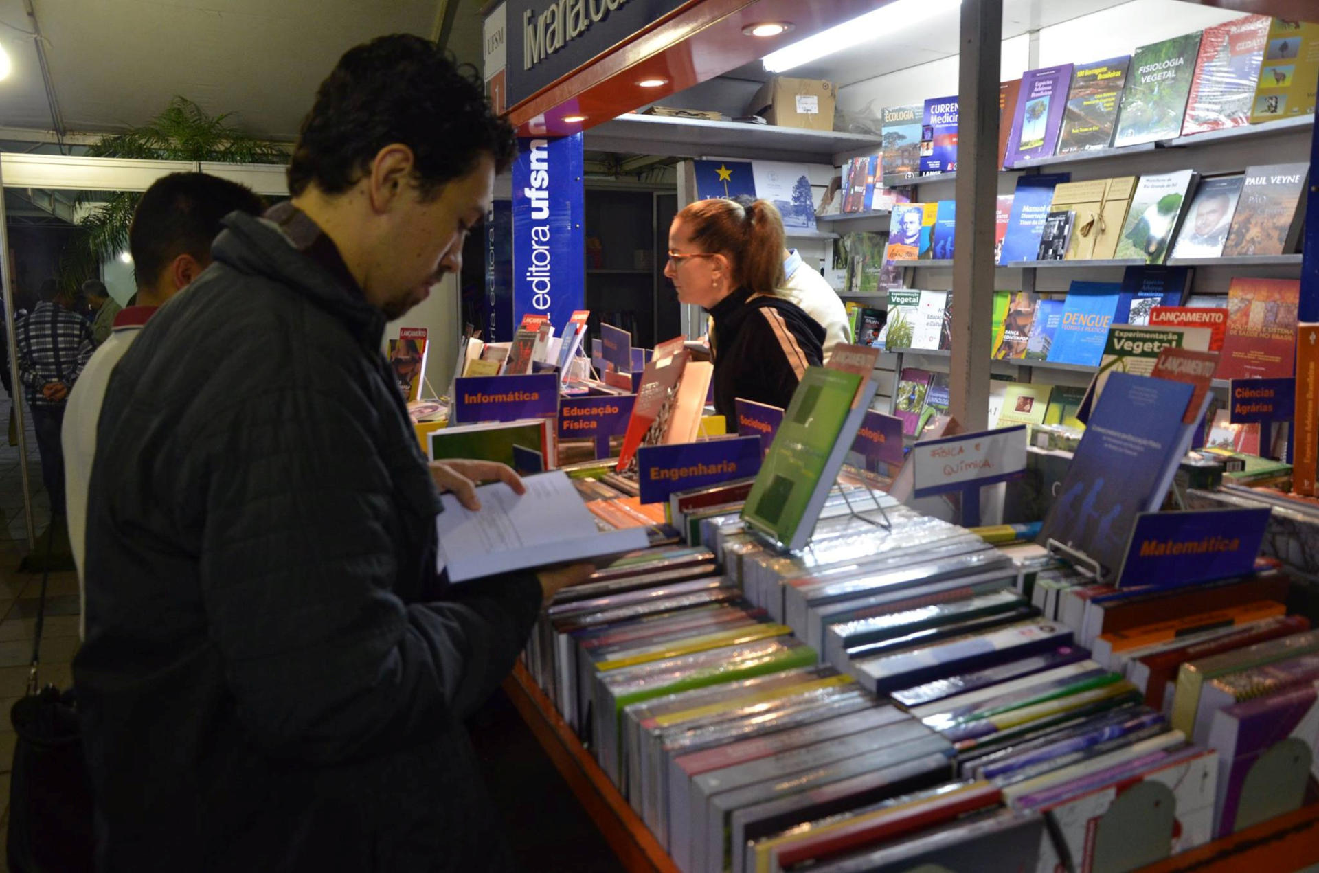 Duas pessoas olhando livros em uma banca da Editora UFSM na Feira do Livro