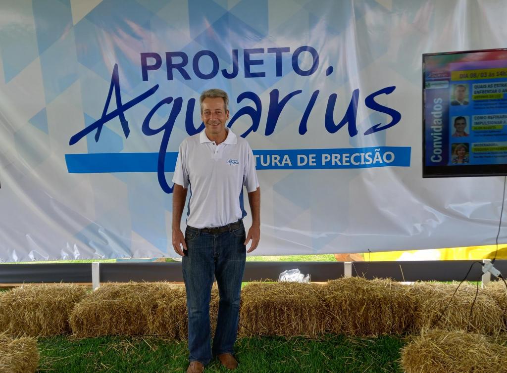 Foto colorida horizontal de homem em pé. Ao fundo, nota-se um banner com a inscrição 'Projeto Aquarius'