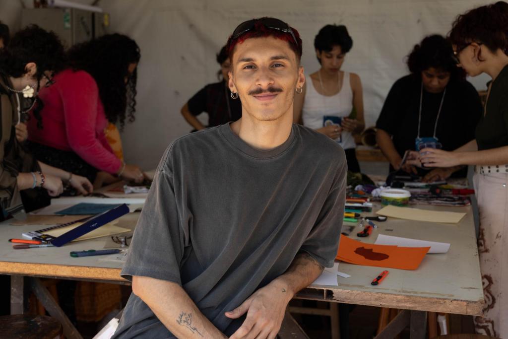 Foto colorida de jovem sentado à frente de uma mesa de desenho