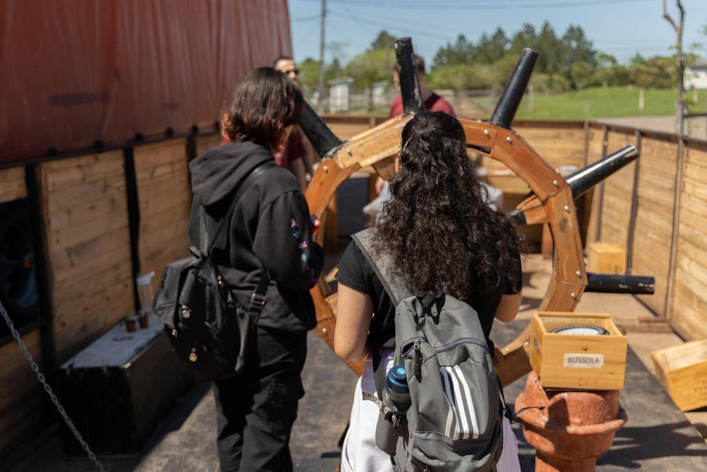 Foto colorida horizontal de duas jovens de costas em um estrutura que simula um barco de madeira