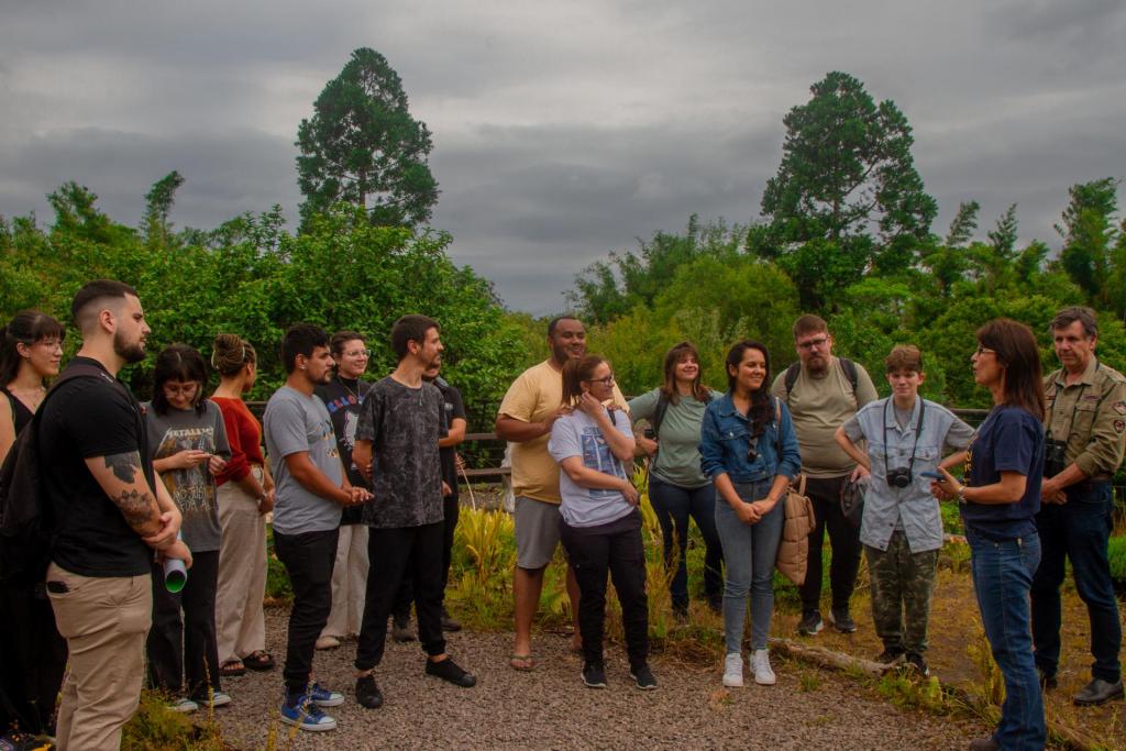 Foto colorida horizontal de um grupo de pessoas reunidas em um espaço com várias árvores em volta