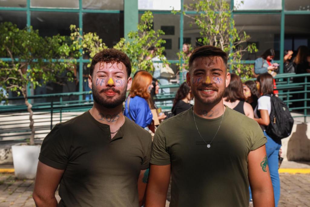 Foto colorida horizontal de dois jovens com os rostos pintados. A imagem mostra os dois do peito para cima. Ao fundo, o prédio do CCR