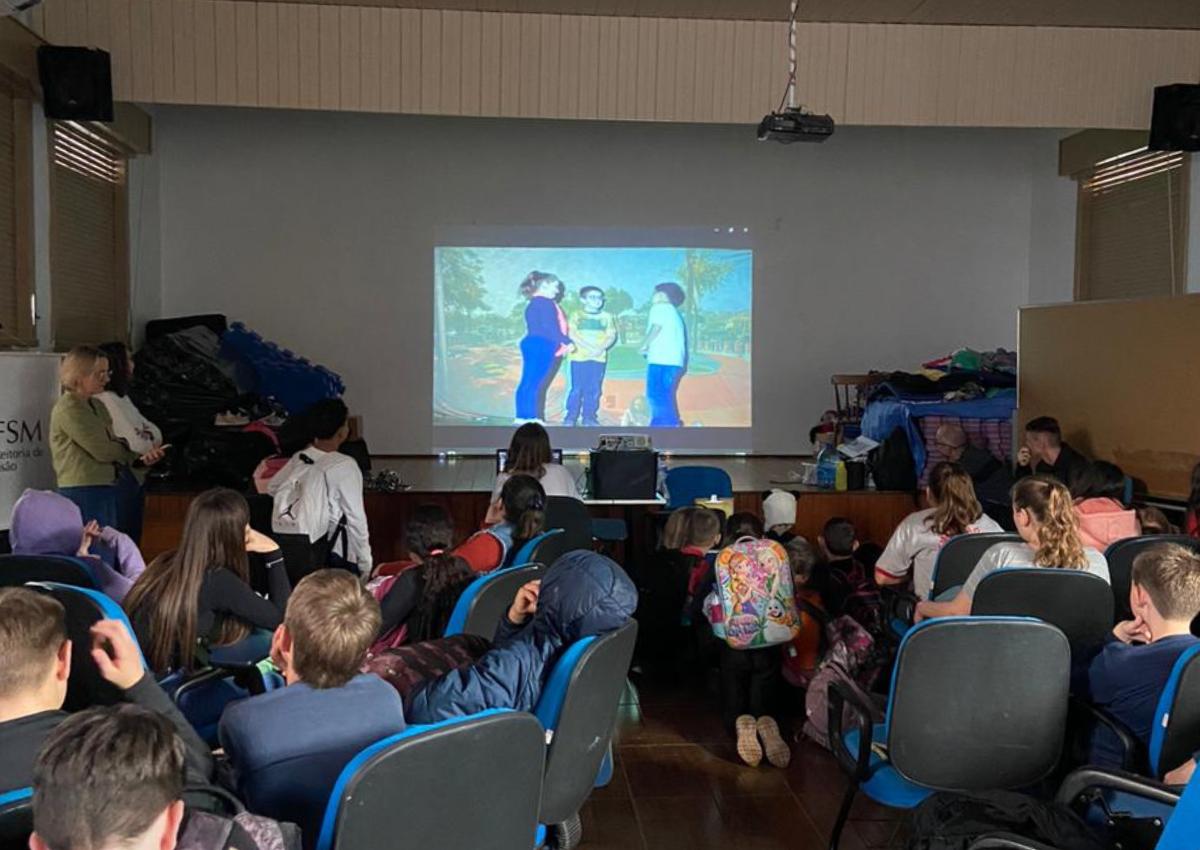 Foto colorida de ação de extensão em escola de Sinimbu. Estudantes aparecem em uma sala fazendo uma encenação em frente a um projeto