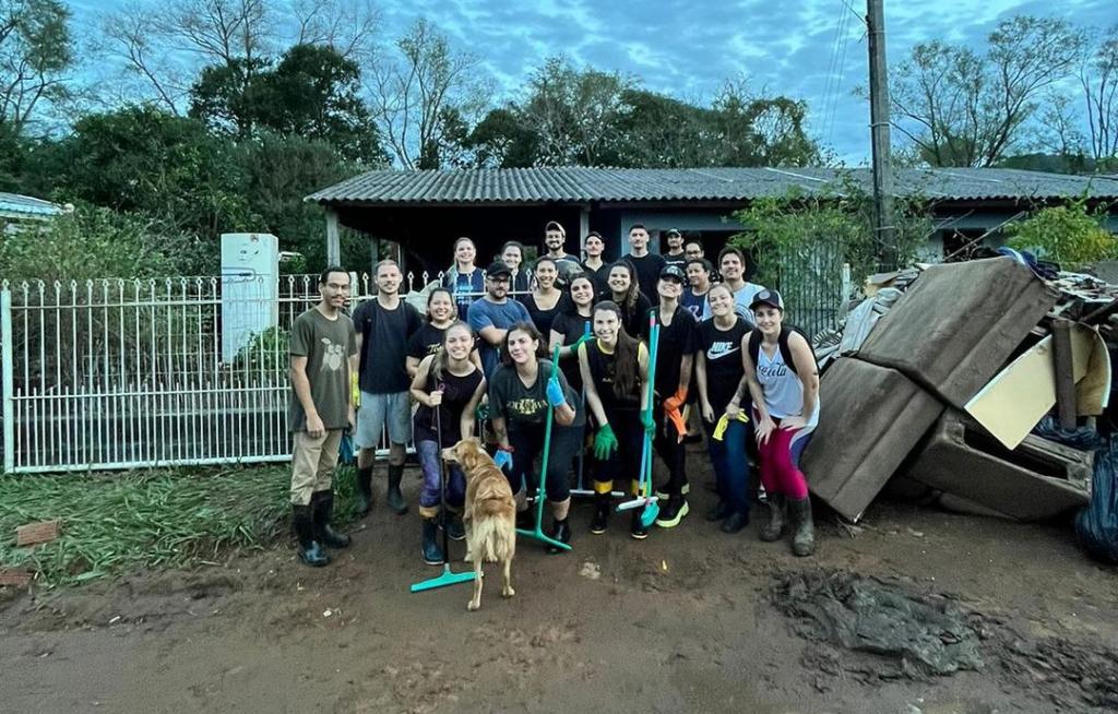 Foto colorida de voluntários em frente a uma casa afetada por enchente