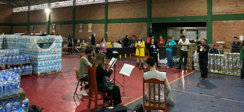 Foto colorida de apresentação da orquestra em abrigo de Santa Maria