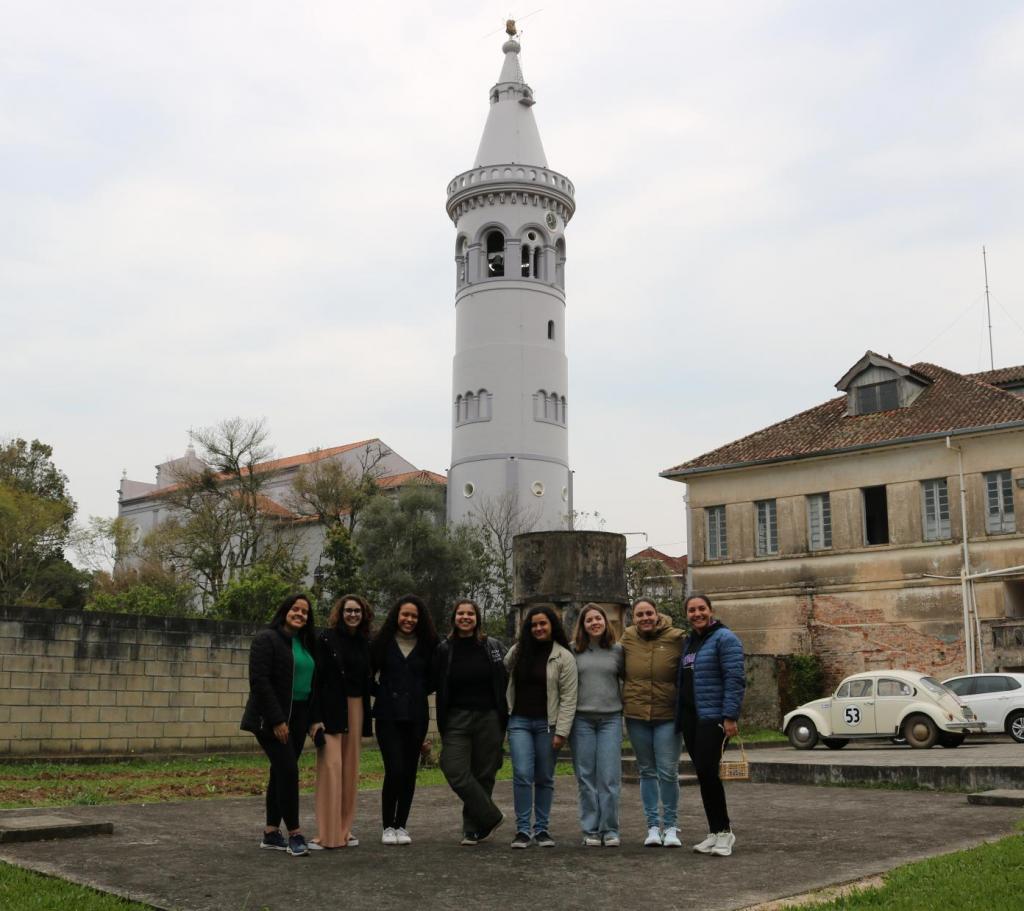 Foto colorida de participantes do projeto. Na imagem, as membras do Ciênciaemflor aparecem de pé e em enfileiradas, posando para foto. Ao fundo, aparece torre de Silveira Martins