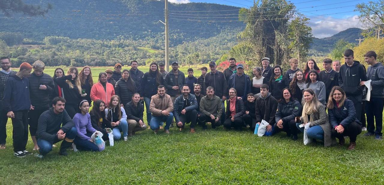 Foto colorida de equipe da UFSM que participou de Dia de Campo em Agudo. Na imagem, diversas pessoas aparecem posando para foto, ao fundo árvores e paisagem rural