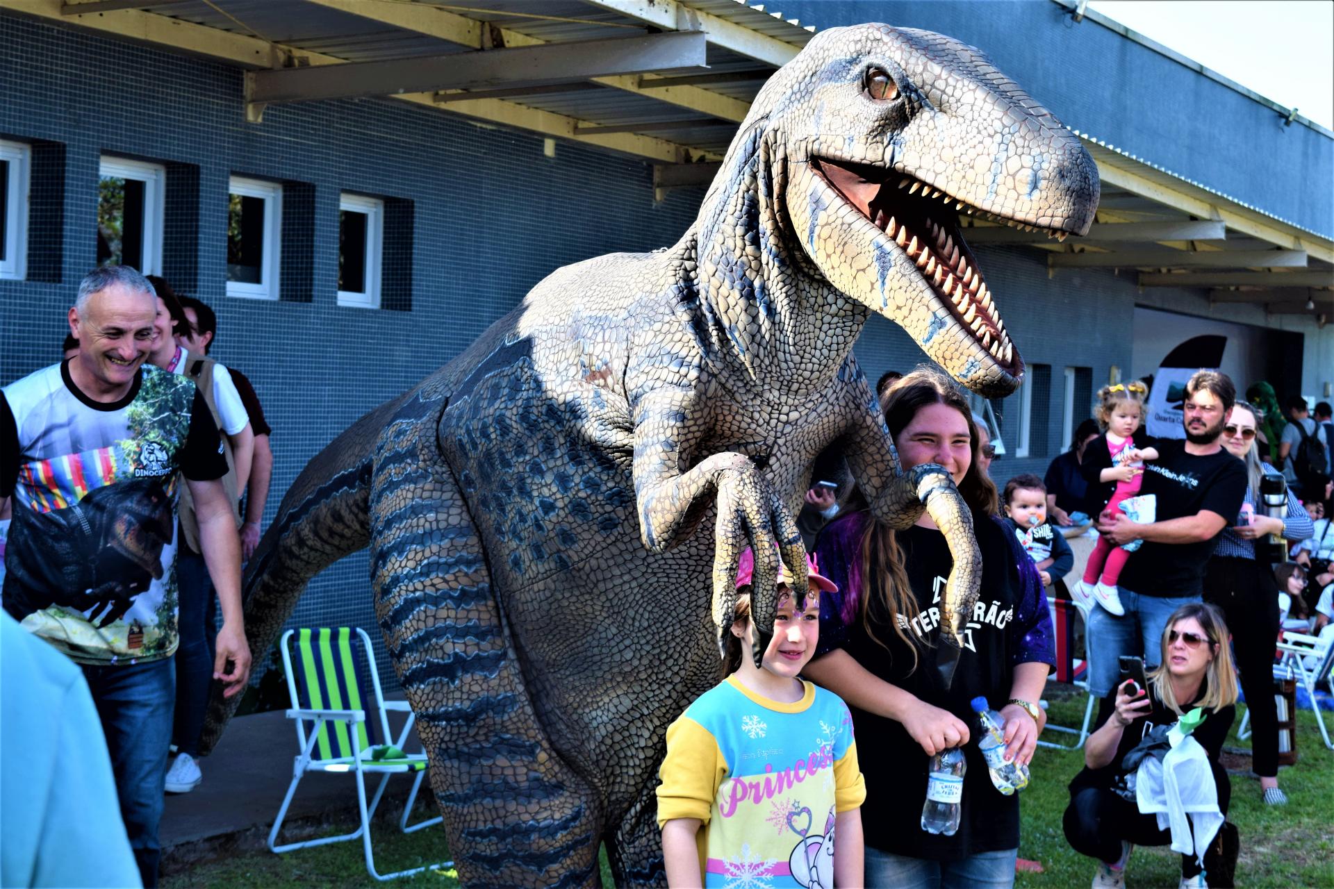 Foto colorida de crianças em frente à representação de um velociraptor realista