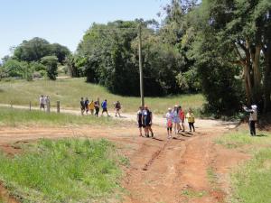 Foto colorida de pessoas em caminhada por estrada no interior de Itaara