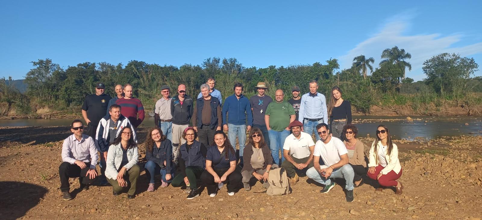 Foto colorida de equipe que participou de atividade de extensão em Paraíso do Sul. As pessoas aparecem perfiladas, com algumas agachadas, enquanto olham para a foto. Ao fundo, céu azul e propriedade rural de Paraíso do Sul