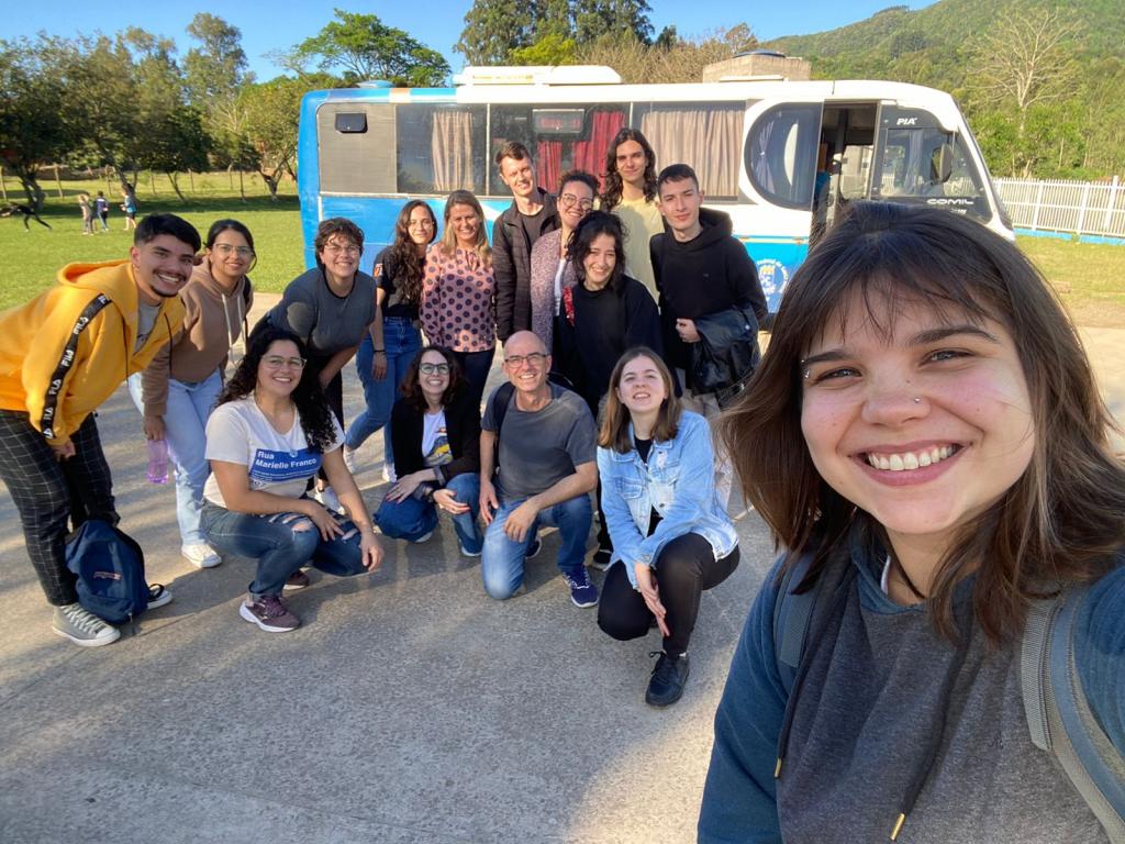 Foto colorida de equipe de voluntários da UFSM em frente a micro-ônibus posando para foto