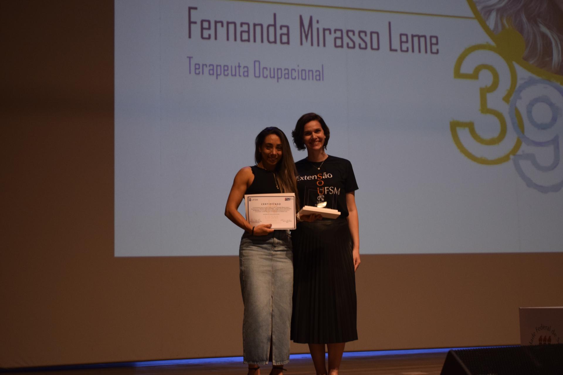 Foto colorida de Fernanda Lemos recebendo placa de Jaciele Sell