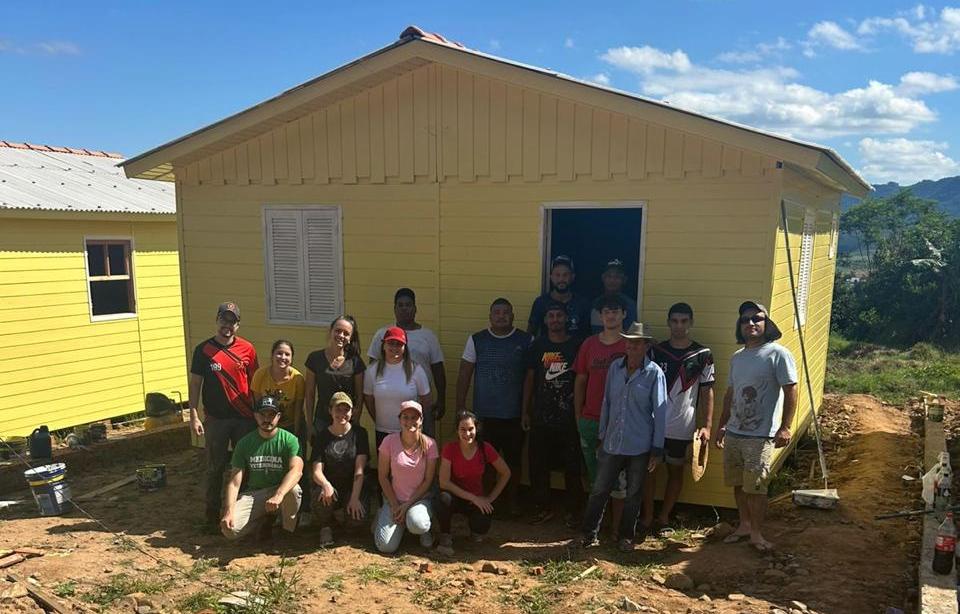 Foto colorida de voluntários da UFSM e do Instituto Renascer em frente à casa pintada na Agrovila Renascer