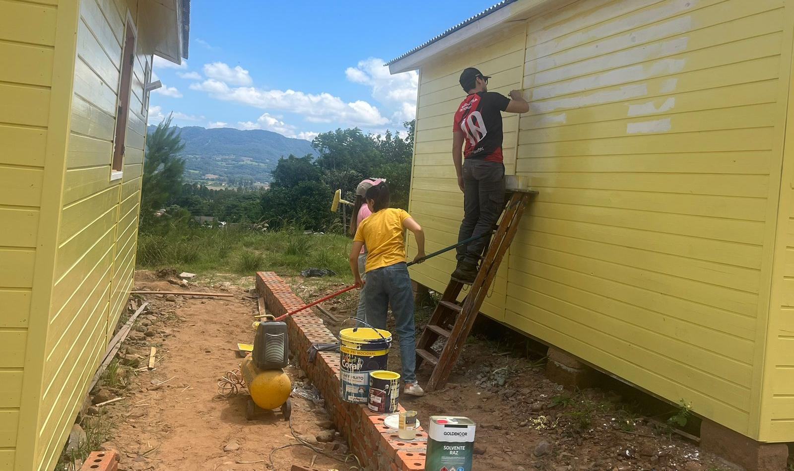 Foto colorida de estudantes da UFSM pintando casa com a cor amarela em Faxinal do Soturno