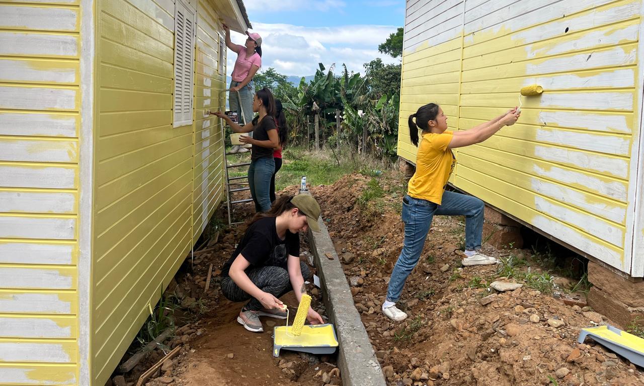 Foto colorida de voluntários pintando casas de madeira com a cor amarela em Faxinal do Soturno