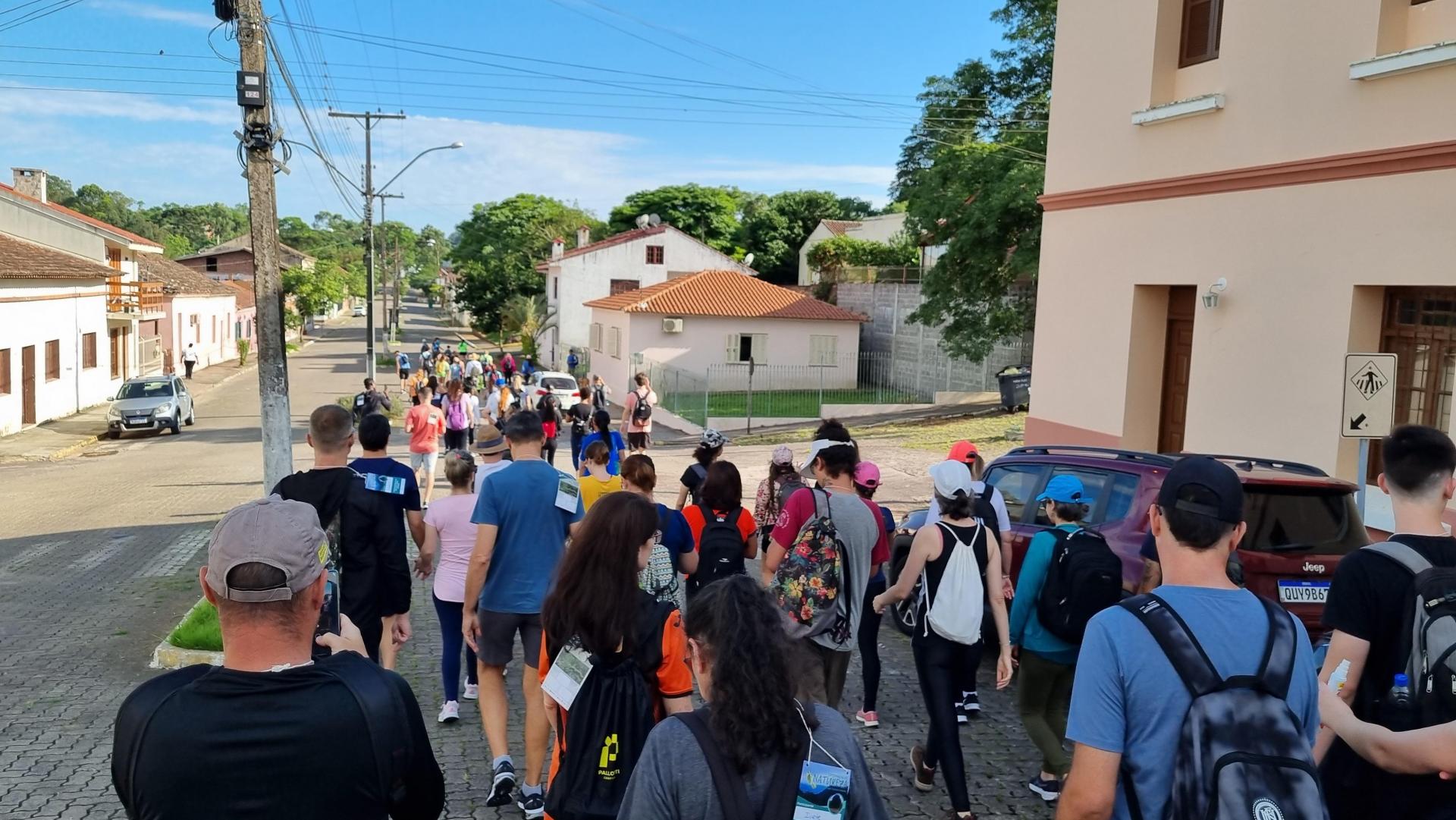 Foto colorida de grupo de pessoas de costas e caminhando em estrada de Silveira Martins