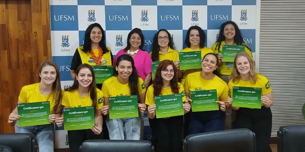 Foto colorida de voluntárias do Projeto Rondon posando para foto com certificados recebidos da vice-reitora da UFSM