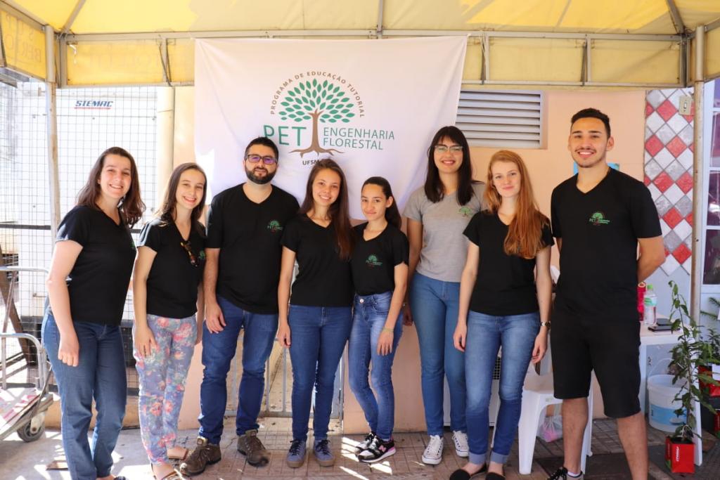 Grupo de 8 estudantes e professores em frente a bandeira do PET Engenharia Florestal