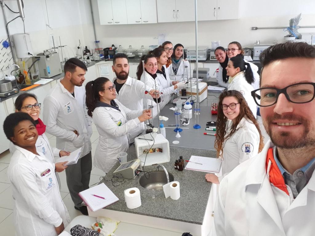 Turma de alunos vestida de jaleco branco trabalhando em laboratório