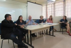 Imagem horizontal tirada do canto da sala. Mesa com os representantes da PROGRAD e PRPGP e Direção do CE. Sentada ao lado direito da mesa a Secretária da Direção.